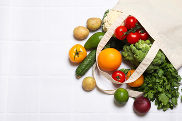 Vegan food delivery. Bag with different fresh vegetables and fruits on white tiled table, flat lay. Space for text