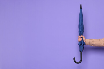 Man holding blue umbrella on purple background, closeup. Space for text © New Africa