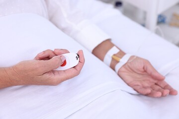 Senior woman pressing emergency call button on bed in hospital, closeup