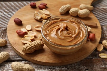 Tasty peanut butter in bowl and groundnuts on wooden table