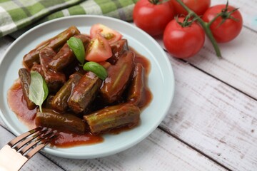 Tasty stew with okra, tomato sauce and basil on white wooden table, closeup. Space for text