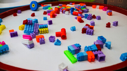A close-up of a white table with scattered colorful plastic building blocks on it, suggesting a playful or educational setting. The blocks represent creativity, learning, and child development.