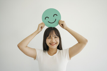 Happy young Asian woman holding smile emoji face, positive mental health, world mental health day...