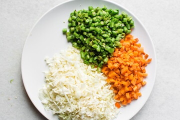 Overhead view of diced carrots green beans and shredded cabbage on a white plate, top view of sliced carrots haricot vert and cabbage on a marble countertop