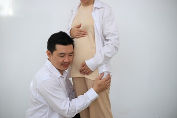 Obraz premium A young man hugs his pregnant wife while standing in a room in his house.