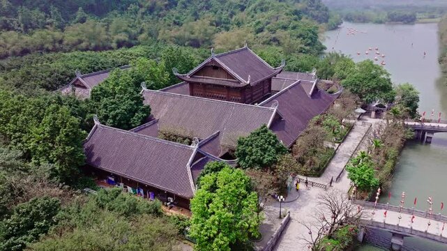 This drone footage captures the majestic architecture of ancient Vietnamese buildings in Tam Coc, Vietnam. The shot highlights the details of the traditional structures, surrounded by lush greenery. 