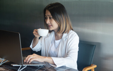 Business woman holding a coffee cup looking at laptop working checking email and  report finance accounting analysis  investment at office