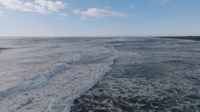 Waves breaking onto endless black sand beach in Iceland, aerial sideways
