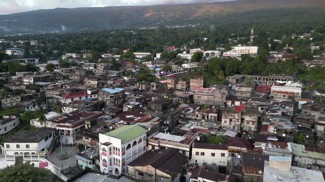Aerial view of Moroni, the capital city of Comoros, showcasing urban buildings, lush greenery, and a mountain in the background.