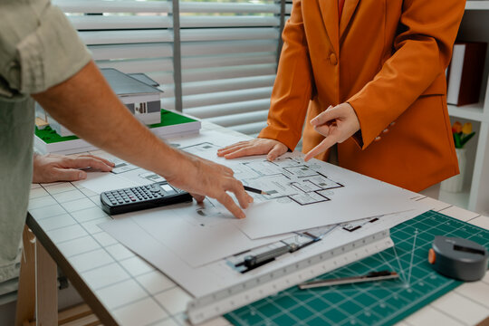 An architect and engineer work as a team, an engineer is discussing with coworker about detail of house model compare with blueprint to make sure it's exactly the same