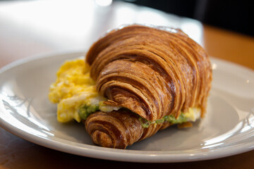 Breakfast of coffee with milk, croissant with guacamole and scrambled egg, poached egg, butter in a roll, ham and cheese, avocado and bacon