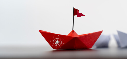 Red paper boat with a compass sails away from a group, representing an entrepreneur taking a new...