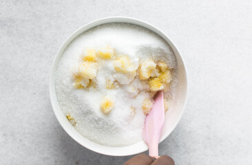 Overhead view of diced pineapple and sugar being mixed together in a white bowl, process of making pineapple cheong or pineapple syrup