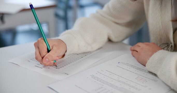 Education, exam and hands with test paper at desk and multiple choice assessment at school. Student, lesson or writing on document for answer, quiz or questionnaire in class for learning evaluation
