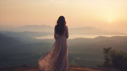 A woman in a flowing dress gazes at the sunset from a mountain viewpoint, surrounded by rolling hills and a tranquil lake