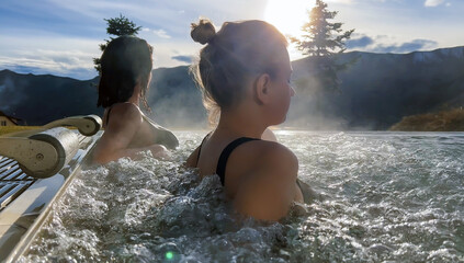 Spa on holidays. Two young women relaxing in outdoor hot pool. Mountain view