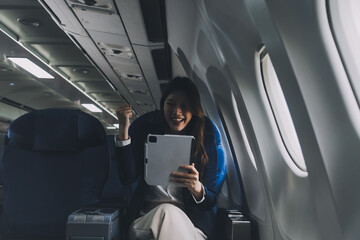 Young Asian executive excels in first class, multitasking with digital tablet, laptop and...