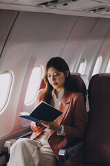 Attractive Asian female passenger of airplane sitting in comfortable seat while working laptop and tablet with mock up area using wireless connection. Travel in style, work with grace.