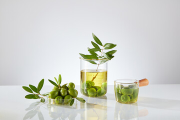 Fresh olives, branches, leaves and olive oil on a decorative jar on a light background. Olive oil is the natural oil extracted from olives, the fruit of the olive tree. Natural ingredient for cosmetic