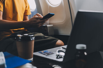 Attractive Asian businesswoman traveling on airplane playing with mobile phone while sitting in cabin.
