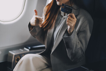 Fototapeta premium Young businesswoman holding credit card near blurred devices in private plane