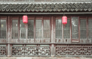 Two red lanterns hang in front of a weathered wooden building with intricately carved latticework and a tiled roof.