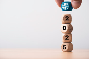 Hand putting blue dartboard with arrow on the top of 2025 year for setup business objective target and goal in new year concept.