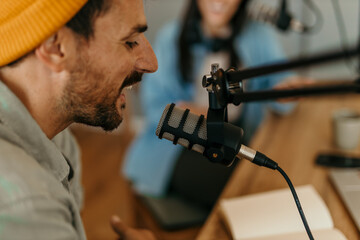 People in the podcast studio talking and recording. Focus on a smiling man with a yellow cap