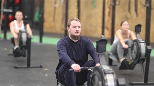 Sportive young man engaged in rowing workout in well-equipped gym during weight training classes