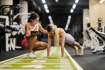 Powerful strong sportswoman doing pushups in a gym with her personal trainer tracking progress on...