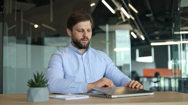 Pleased office male worker stretching back and breathing out while sitting by desktop with laptop and diary. Financial manager relaxing after completed job close laptop indoors.