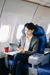Young Asian executive excels in first class, multitasking with digital tablet, laptop and...