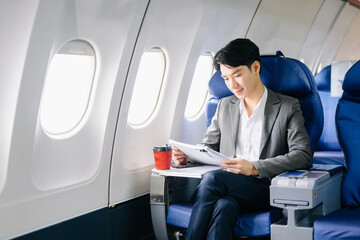 Young Asian executive excels in first class, multitasking with digital tablet, laptop and smartphone.