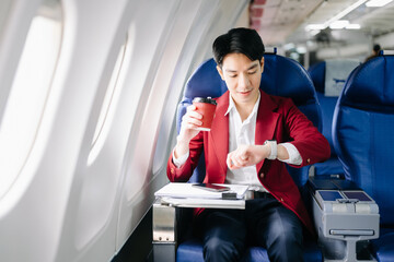 Young Asian executive excels in first class, multitasking with digital tablet, laptop and...