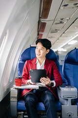 Young Asian executive excels in first class, multitasking with digital tablet, laptop and...