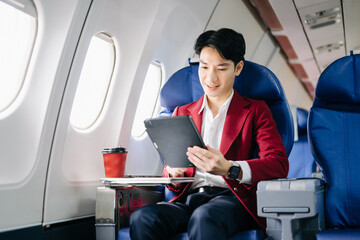 Young Asian executive excels in first class, multitasking with digital tablet, laptop and...