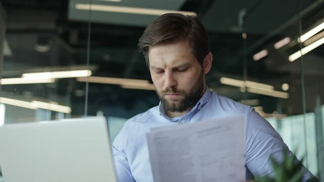 Businessman feeling stressed while reviewing paperwork at his desk in the office.