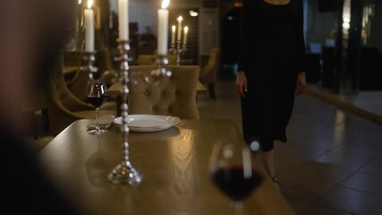 A woman in an evening dress comes to a restaurant on a date with a man who is waiting for her. A young couple comes to a restaurant. A girl approaches a man at a table.