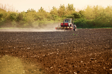 Agricultural land is cultivated by a tractor, sowing seeds.