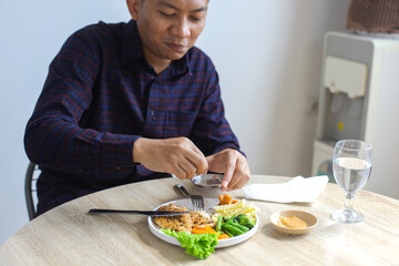 Cheerful Asian Man Adding Spices Into Chicken Steak While Eating