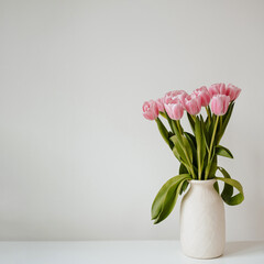 Pink tulip flowers in a clay vase on a table against white background. Soft light, neutral tones. Clean minimalist style with aesthetic vibe