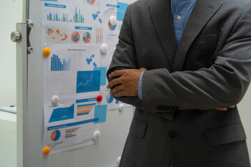 Fototapeta premium A male businessman explains graphs on a board during a meeting. He discusses marketing and finance strategies with the team, focusing on key data points to drive informed business decisions growth.