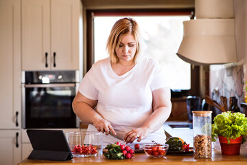Overweight woman in the kitchen, making homemade lunch. Choosing healthy food, making and eating vegetable salad.