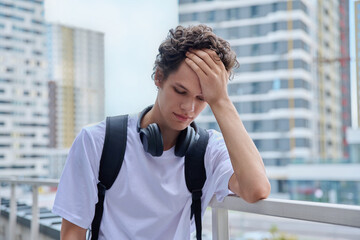 Upset sad unhappy young male outdoor, modern skyscrapers urban style