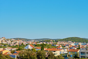 Obraz premium View on coastal town with red roofed houses and lush green hills under clear blue sky. Touristic Mediterranean town near Adriatic sea for summer holidays