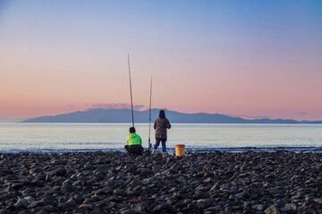 People fishing along the shoreline of the Firth of Thames at sunset at Orere Point, Auckland, New...