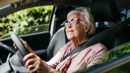 Happy senior woman driving car alone, enjoying car ride. Safe driving for elderly adults, older...