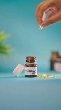 VERTICAL VIDEO OF HAND TAKING OUT TRIPHALA TABLETS FROM MEDICINE BOTTLE