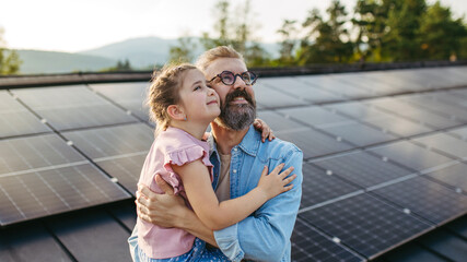 Father with girl on roof with solar panels, hugging, looking at the sky. Rooftop solar or photovoltaic system. Sustainable future for next generation.