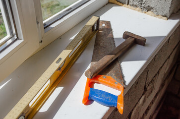 Construction tools on the window sill , hand saw , level meter